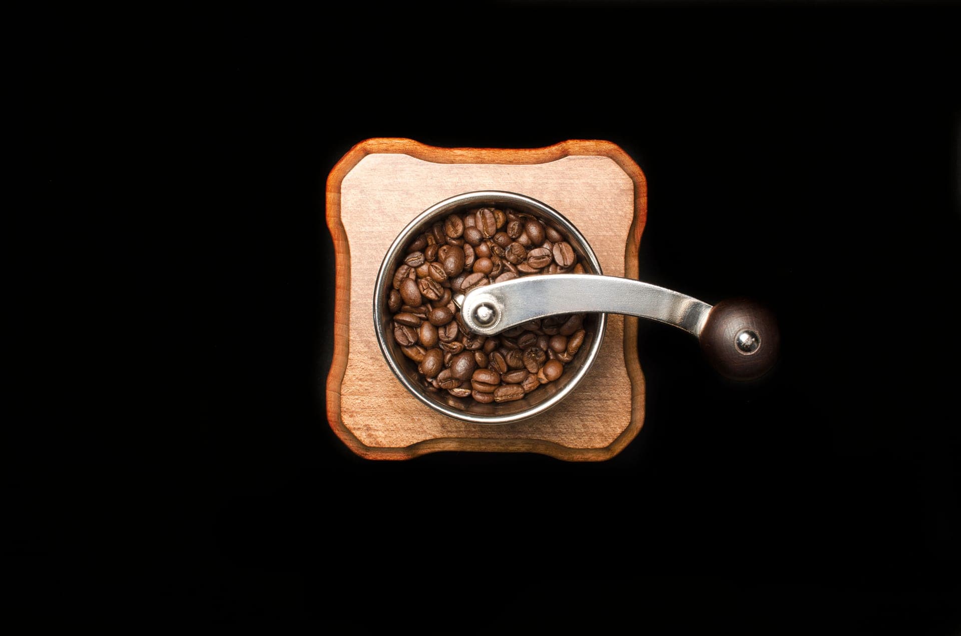 A hand coffee grinder and fresh grounds in warm light on a dark surface