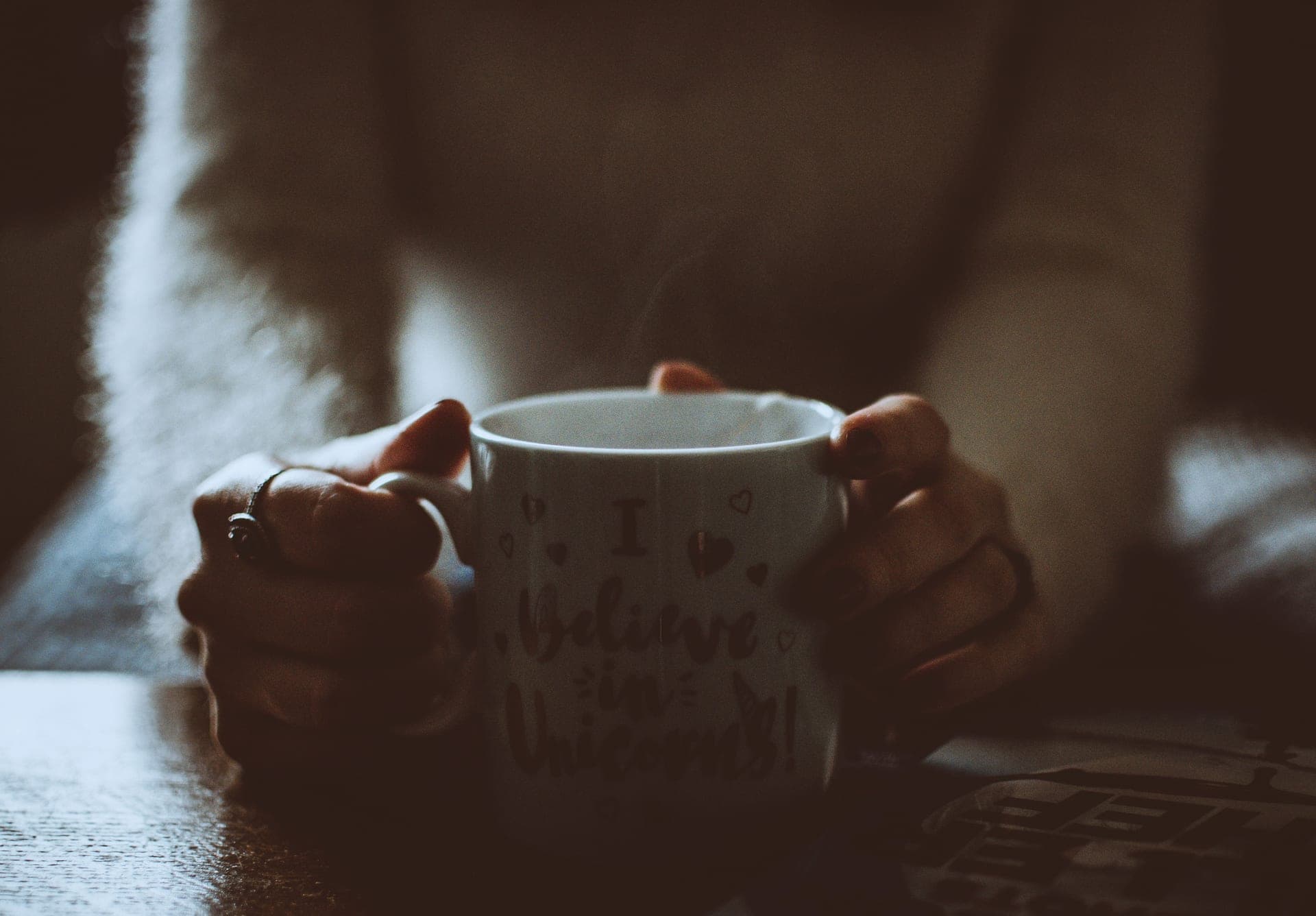 A steaming mug of coffee held in two hands against a dark background